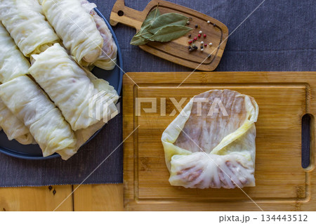 Process of making homemade stuffed cabbage rolls with minced meat, rice and spices in a cozy home kitchen. Traditional comfort food preparation, step by step cooking concept. 134443512