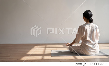 明るい日差しが差し込む清潔感のある室内でヨガマットの上に座り瞑想する女性の後ろ姿 明るい日差しが差し込む清潔感のある室内でヨガマットの上に座り瞑想する女性の後ろ姿 134443688