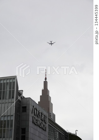 東京 新宿駅南口からの都市風景 ビルの上にジェット旅客機が見える 134445399
