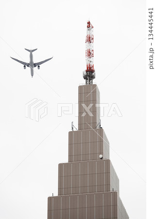 高層ビル上部に設置されているアンテナとジェット旅客機 134445441