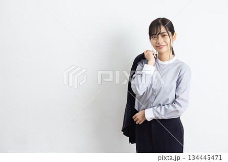 白い壁の前でジャケットを肩にかけて微笑む若いビジネスウーマン 白い壁の前でジャケットを肩にかけて微笑む若いビジネスウーマン 134445471