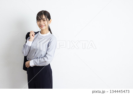 白い壁の前でジャケットを肩にかけて微笑む若いビジネスウーマン 白い壁の前でジャケットを肩にかけて微笑む若いビジネスウーマン 134445473