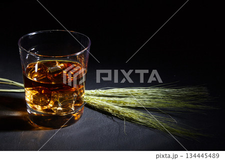 a glass of whiskey with ice and rye ears on a black stone table. 134445489