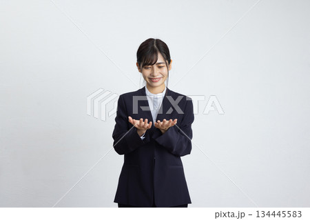 白い壁の前で胸の前に手を出して微笑む若いビジネスウーマン 134445583