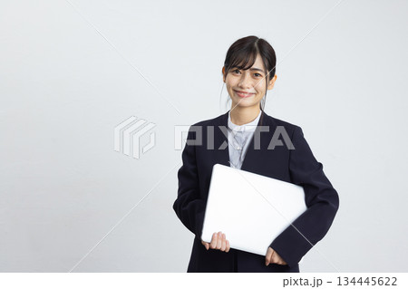 ノートパソコンを抱えて白い背景の前で微笑む若いビジネスウーマン 134445622