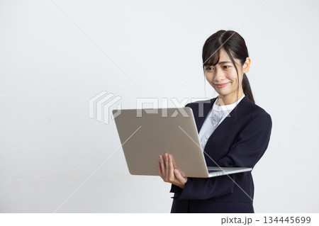 白い壁の前でパソコンを操作する若いビジネスウーマン 白い壁の前でパソコンを操作する若いビジネスウーマン 134445699