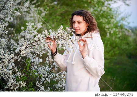 Woman allergic enjoying after treatment from seasonal allergy at spring. Portrait of young woman sniffing the flowers in front of blossom tree at springtime. Spring allergy concept. Woman allergic enjoying after treatment from seasonal allergy at spring. Portrait of young woman sniffing the flowers in front of blossom tree at springtime. Spring allergy concept. 134446273