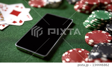 Smartphone showing black screen lying on green poker table with playing cards and chips 134446862