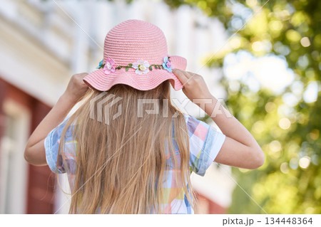 Caucasian young girl wearing a floral pink hat in a sunny outdoor setting 134448364