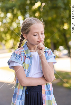 Thoughtful caucasian young girl in colorful shirt outdoors on a sunny day 134448368