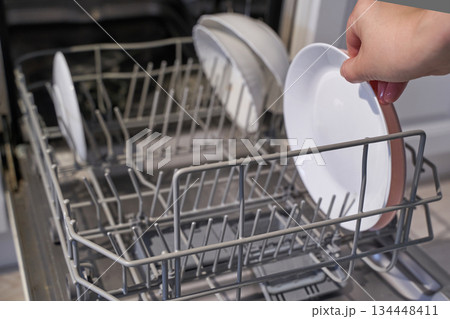 Person loading dishwasher with plates in kitchen setting Person loading dishwasher with plates in kitchen setting 134448411