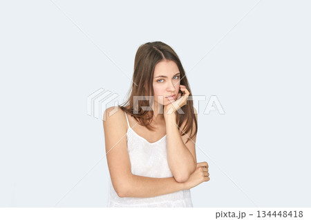 Young caucasian female in white top with hand on face looking pensive against 134448418