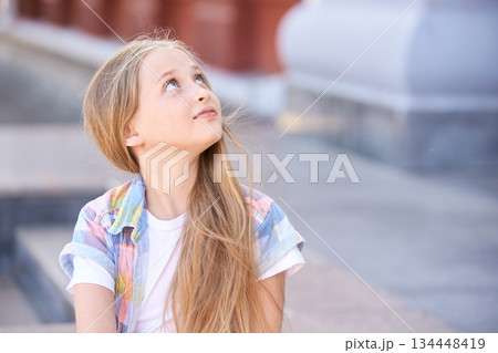 Caucasian young girl with long blonde hair looking upwards outdoors in casual Caucasian young girl with long blonde hair looking upwards outdoors in casual 134448419