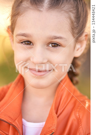 Smiling caucasian young girl in orange jacket outdoors with blurred background Smiling caucasian young girl in orange jacket outdoors with blurred background 134448421