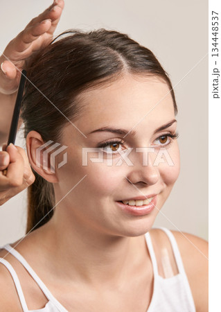 Young caucasian female enjoying hair styling by hairdresser with comb in bright Young caucasian female enjoying hair styling by hairdresser with comb in bright 134448537