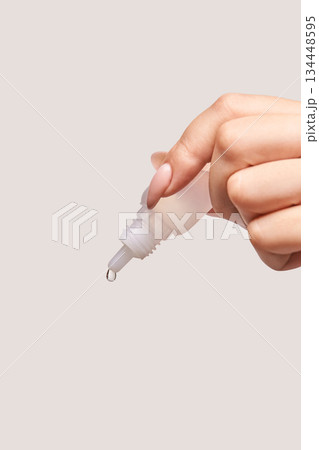 Close-up of female hand dispensing liquid from dropper bottle against neutral 134448595