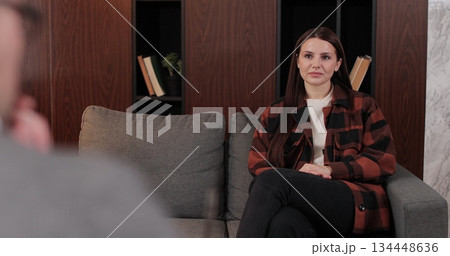 Over shoulder view of man psychologist sitting in armchair, talking with upset woman patient. Psychologist taking notes on clipboard. Psychology, mental therapy, mental health, therapy session. Over shoulder view of man psychologist sitting in armchair, talking with upset woman patient. Psychologist taking notes on clipboard. Psychology, mental therapy, mental health, therapy session. 134448636