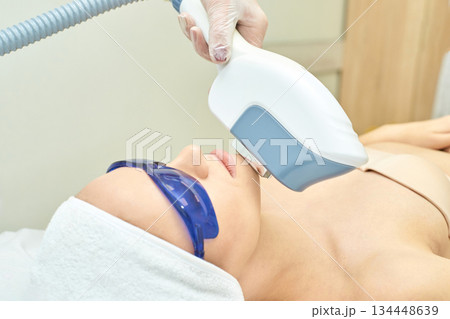 Young caucasian female receiving laser facial treatment in a beauty clinic Young caucasian female receiving laser facial treatment in a beauty clinic 134448639