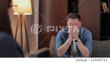 Man gets mental care treatment, man visits psychotherapist, sitting on the sofa talking with doctor, suffering expression. Daily lifestyle concept. Man gets mental care treatment, man visits psychotherapist, sitting on the sofa talking with doctor, suffering expression. Daily lifestyle concept. 134448712