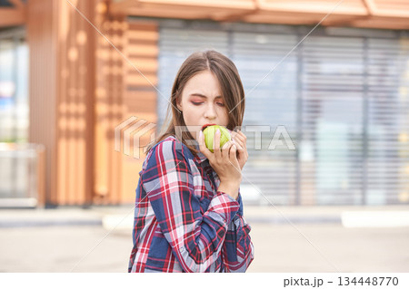Young caucasian female enjoying fresh green apple outdoors in casual plaid Young caucasian female enjoying fresh green apple outdoors in casual plaid 134448770