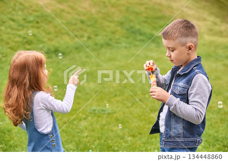 Caucasian children playing with bubbles on grass in casual clothing on a sunny 134448860