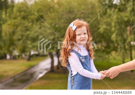 Young caucasian redhead girl holding hands outdoors in green park setting 134448889