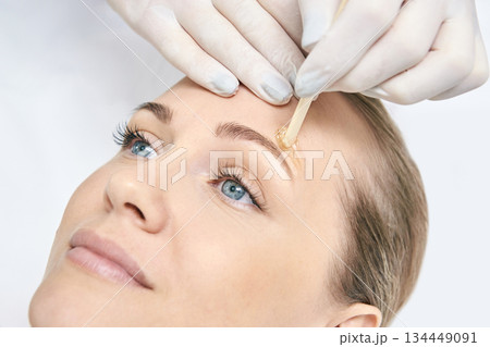 Caucasian female receiving eyebrow waxing treatment close-up with applicator 134449091