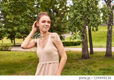 Caucasian female adult smiling in beige dress outdoors in a green park 134449116