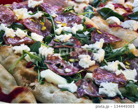 Fresh pizza topped with salami, cheese, and greens served on a wooden table in a busy restaurant 134449303