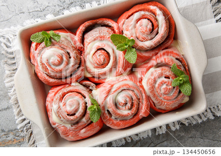 Festive pink cinnabons, cinnamon rolls with white icing, close-up in a baking pan. Horizontal top view 134450656