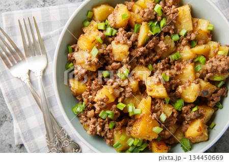 Fried potatoes with ground beef and green onions close-up in a plate. Horizontal top view 134450669