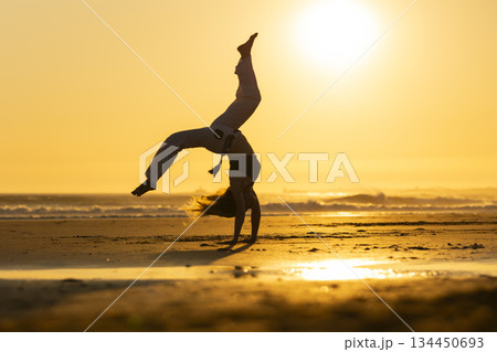 Woman performing capoeira cartwheel on beach at sunset 134450693