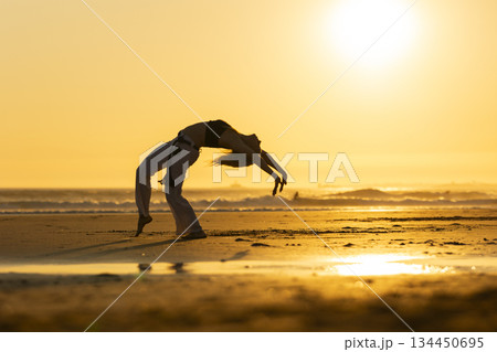 Capoeira artist performing flexible movement on beach at sunset 134450695