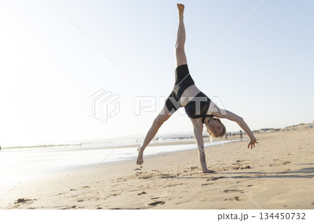 Woman performing cartwheel on beach sand 134450732