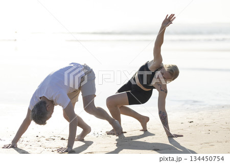 Couple practicing yoga dynamic moves on beach Couple practicing yoga dynamic moves on beach 134450754