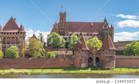 Malbork Castle, a brick Gothic castle in northern Poland, Europe. Magnificent medieval castle, a testament to history and architecture, stands proudly against a backdrop of blue sky and lush greenery. Malbork Castle, a brick Gothic castle in northern Poland, Europe. Magnificent medieval castle, a testament to history and architecture, stands proudly against a backdrop of blue sky and lush greenery. 134453037