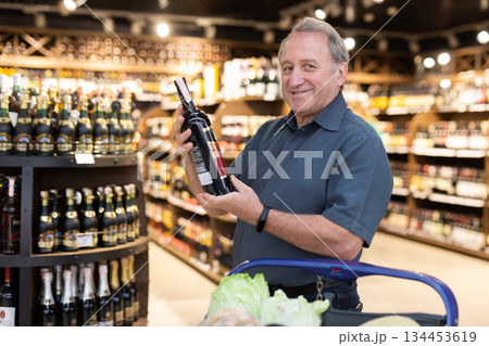 Mature man choosing nice bottle of wine in supermarket Mature man choosing nice bottle of wine in supermarket 134453619