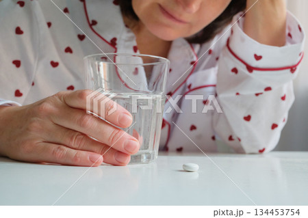 Woman feeling unwell experiencing headache, preparing to take medication from table at home 134453754