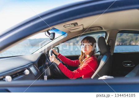 青空のもと運転席に乗る赤いニットのセーターを着た若いロングヘアの女性 134454105