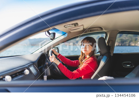 青空のもと運転席に乗る赤いニットのセーターを着た若いロングヘアの女性 134454106