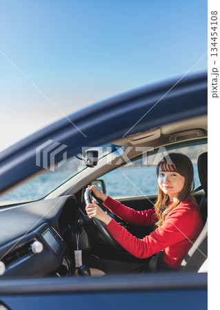 青空のもと運転席に乗る赤いニットのセーターを着た若いロングヘアの女性 134454108