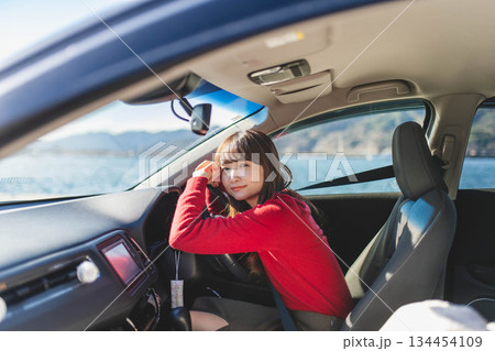 青空のもと運転席に乗る赤いニットのセーターを着た若いロングヘアの女性 134454109