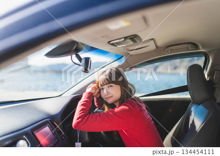 青空のもと運転席に乗る赤いニットのセーターを着た若いロングヘアの女性 134454111