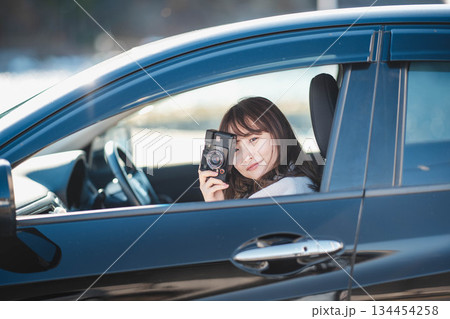 車の助手席に座りカメラを構える若いロングヘアの女性 車の助手席に座りカメラを構える若いロングヘアの女性 134454258