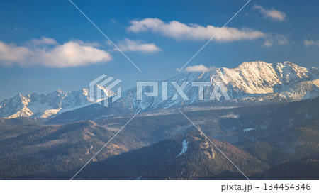Tatra Mountains above Zakopane town in Poland, Europe. Panoramic views of a rugged mountain range with snow-dusted peaks under a bright blue sky, a tranquil and majestic landscape. 134454346