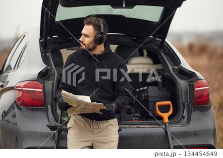 With map in hands, near automobile. Man is with metal detector in the field With map in hands, near automobile. Man is with metal detector in the field 134454649