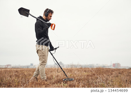 Holding a shovel. Man is with metal detector in the field 134454699