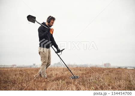 Holding a shovel. Man is with metal detector in the field Holding a shovel. Man is with metal detector in the field 134454700