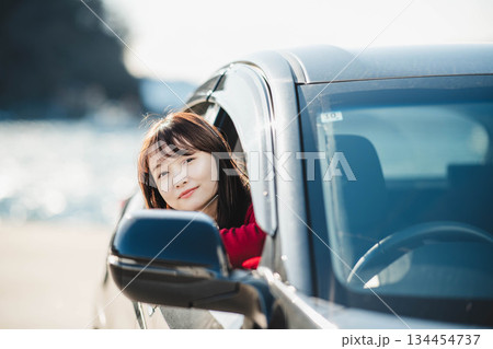 車に乗りながら座席から身を乗り出す赤いニットの若い女性 134454737