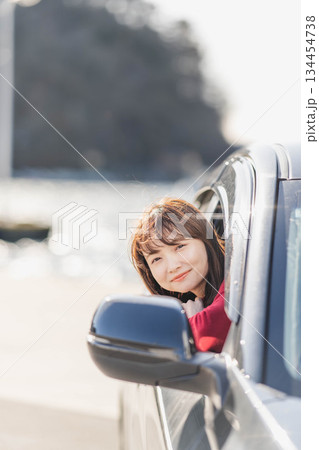 車に乗りながら座席から身を乗り出す赤いニットの若い女性 車に乗りながら座席から身を乗り出す赤いニットの若い女性 134454738